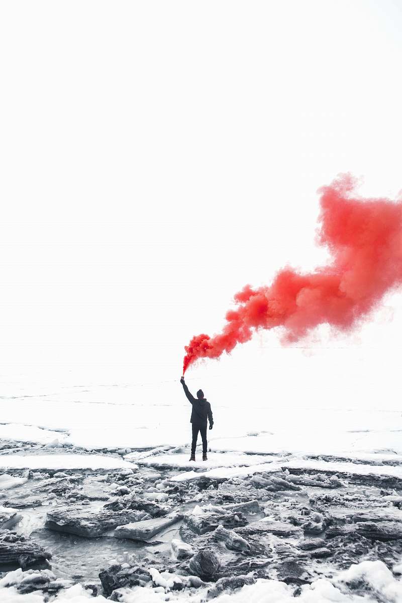 smoke selective color photography of person holding orange gas smoke standing on snow red