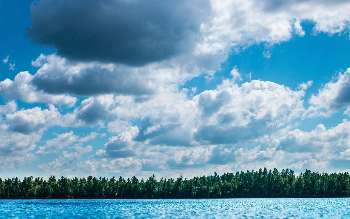 cloud green trees across blue body of water under cloudy sky clouds