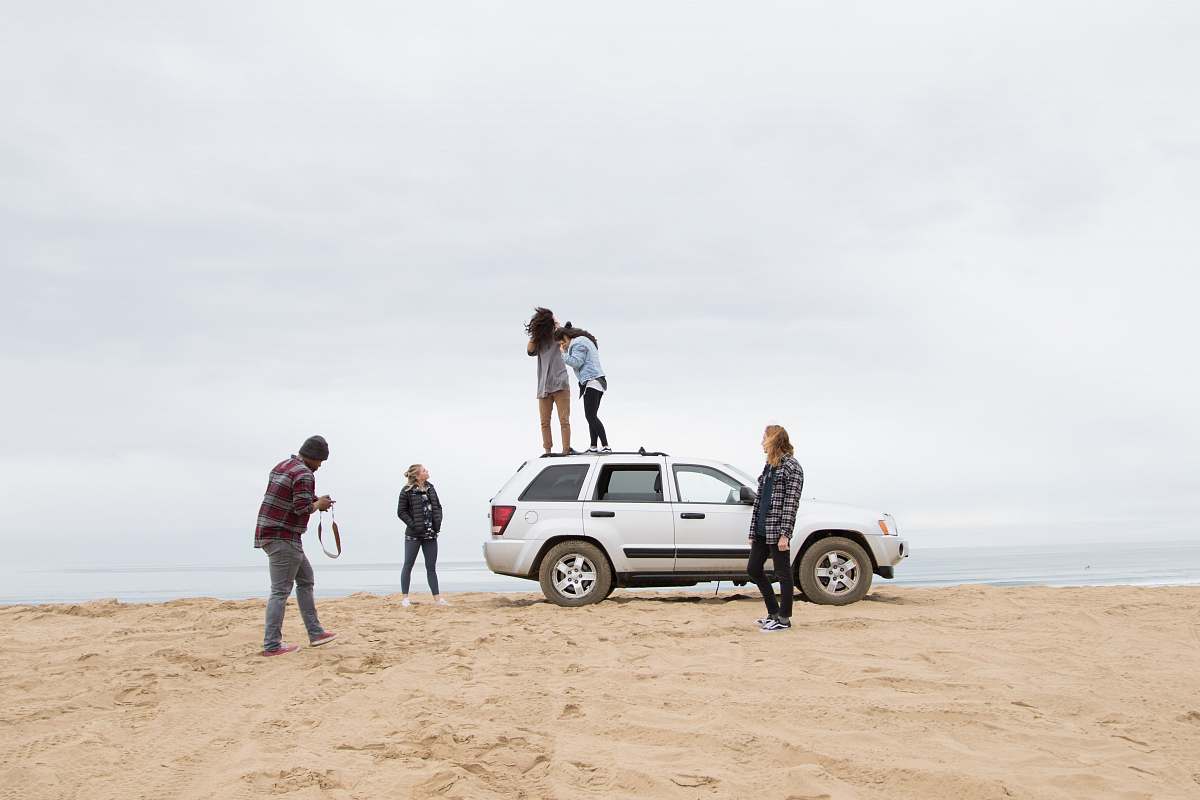 car two people standing on Jeep Grand Cherokee SUV while the other person camera on sand during daytime transportation