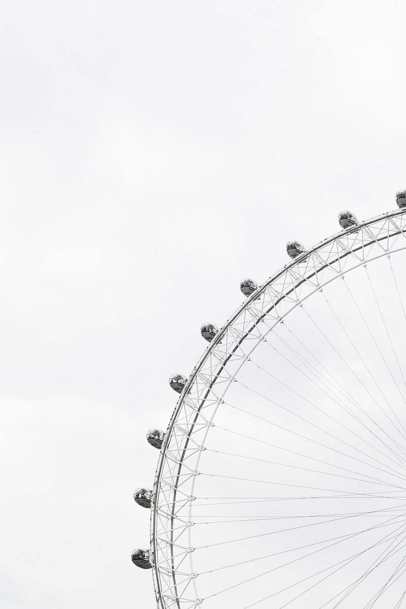 black-and-white Part of a ferris wheel with enclosed cars for riding in and people in the cars against an overcast sky minimal