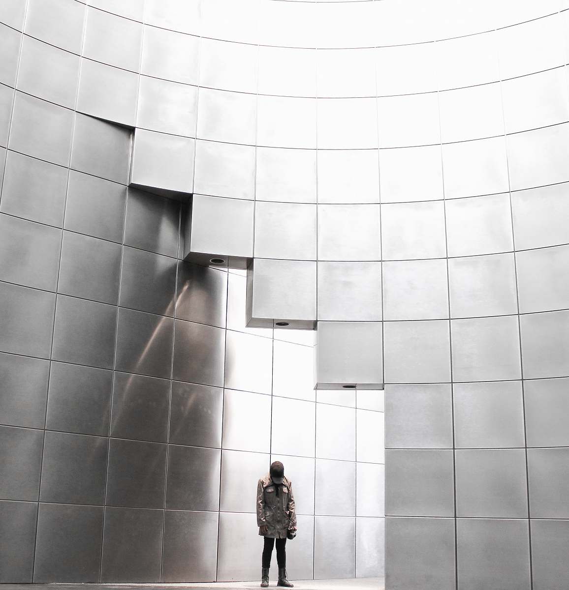 black-and-white person standing under metal block building wall