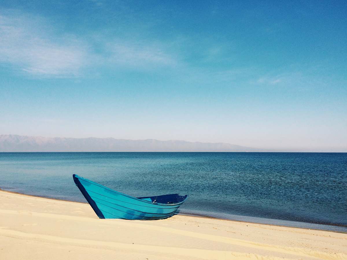 water blue boat on sand near body of water during daytime ocean