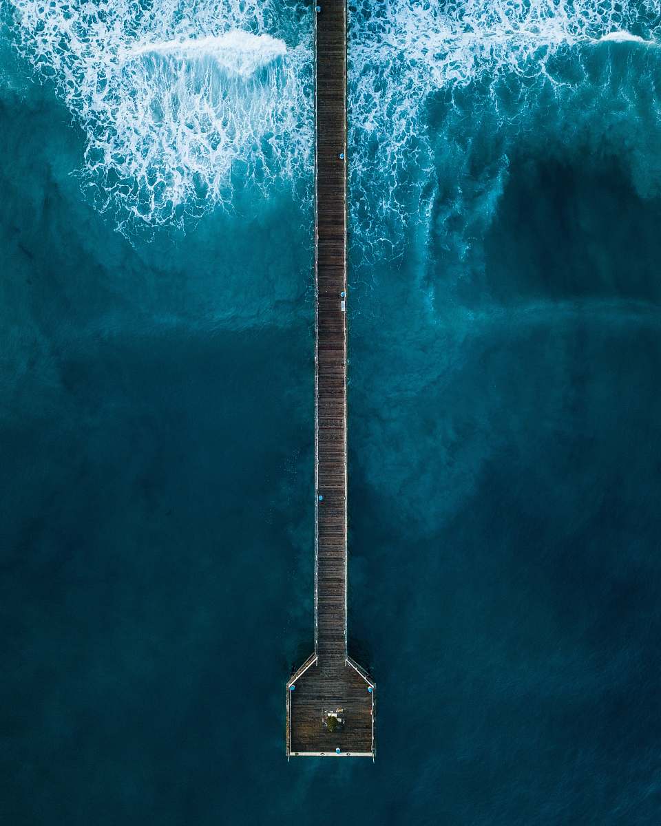 sea aerial photography of person standing on dock beside sea at daytime water
