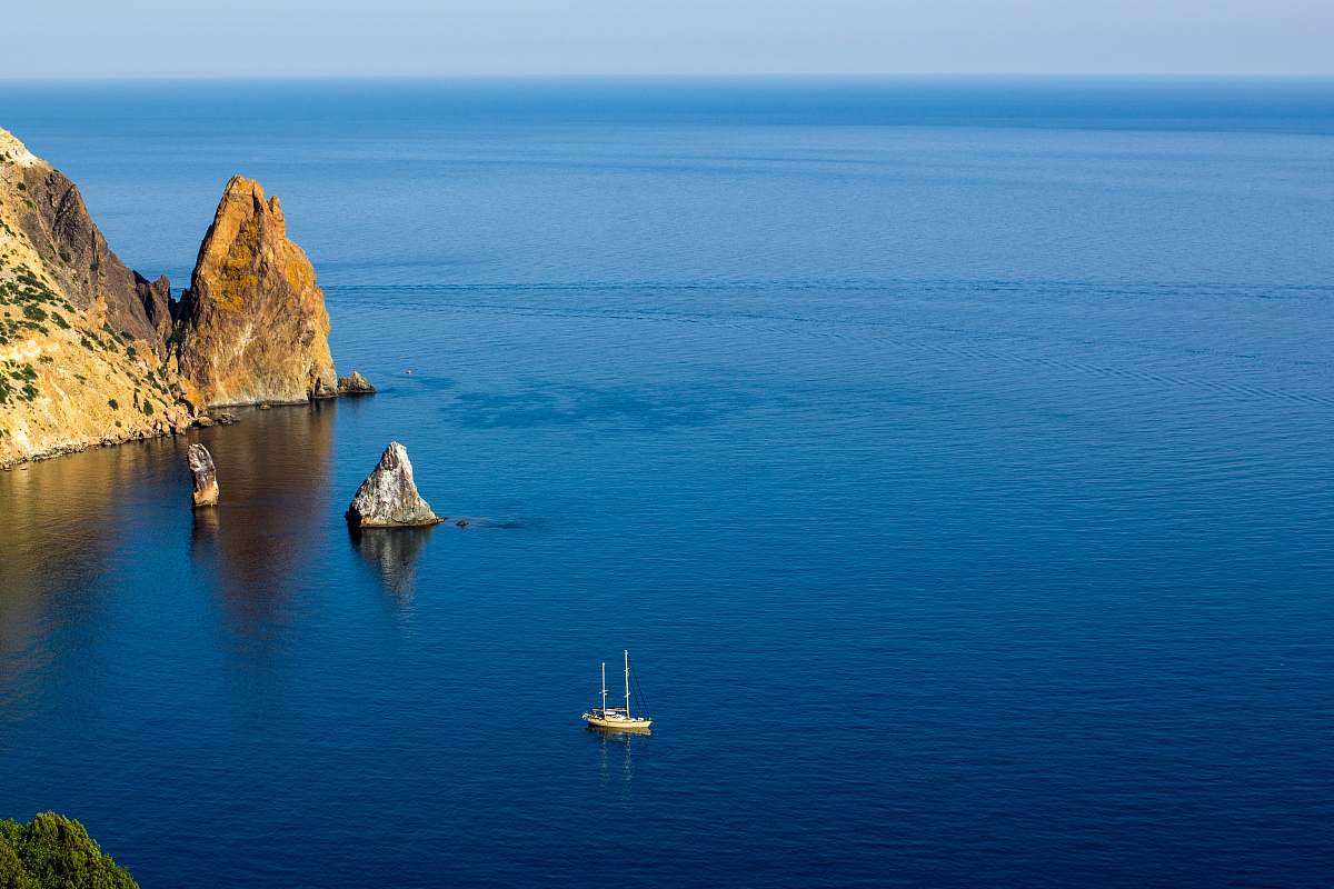 sea aerial photography of white ship on sea near rock formations under blue sky during daytime water