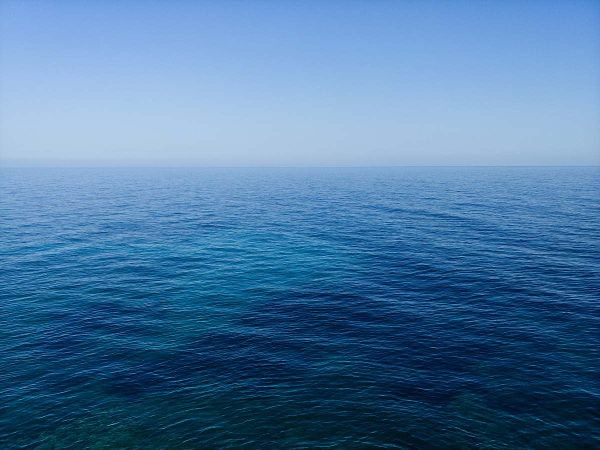 water calm body of water under blue sky photography during daytime sea