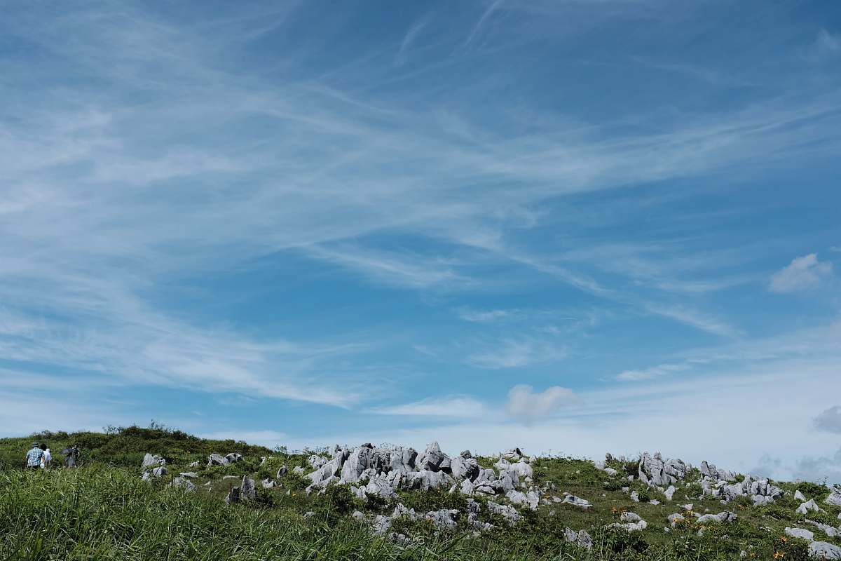 nature green hill with rocks under white clouds and blue sky during daytime outdoors