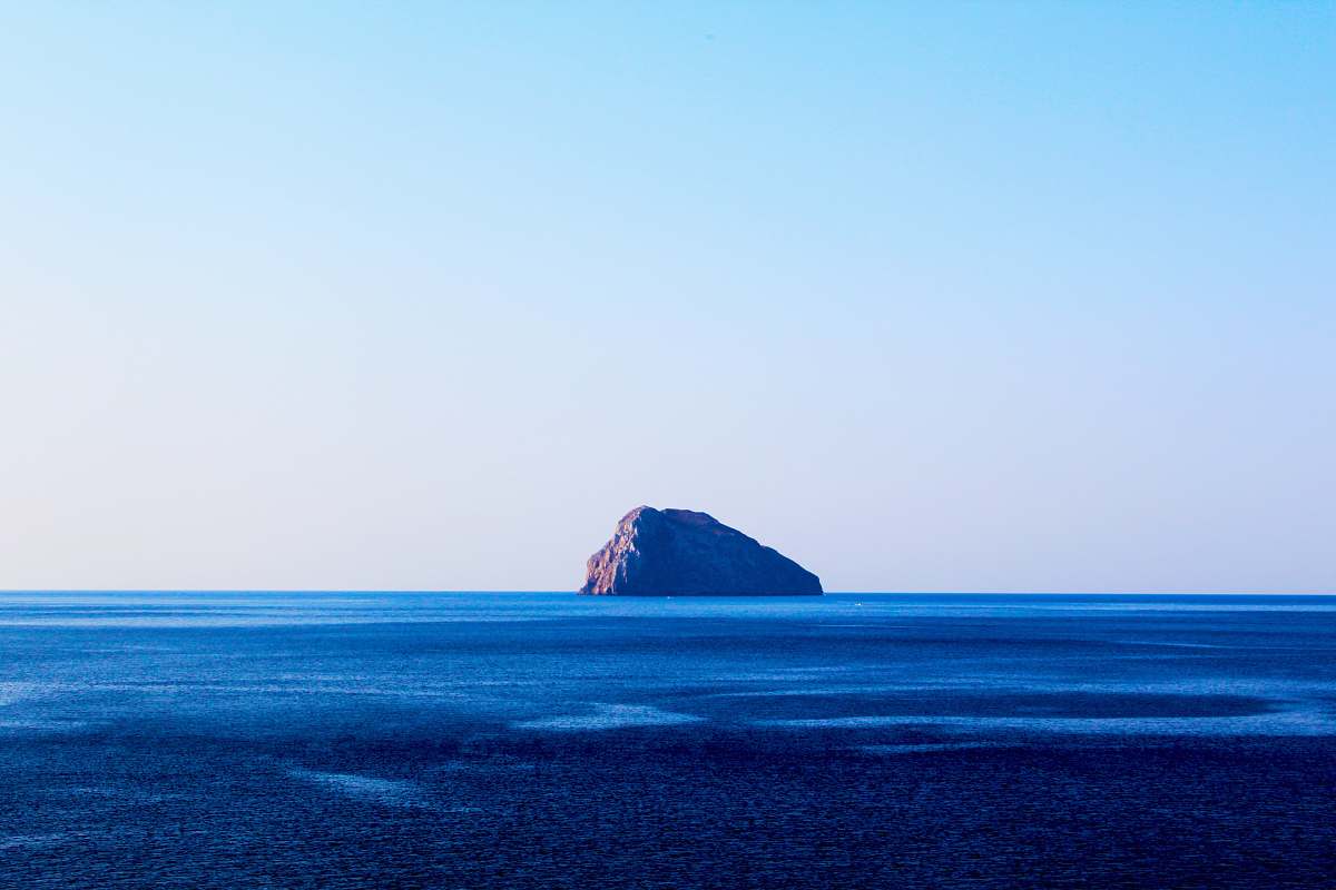 sea islet on body of water under cumulus clouds ocean