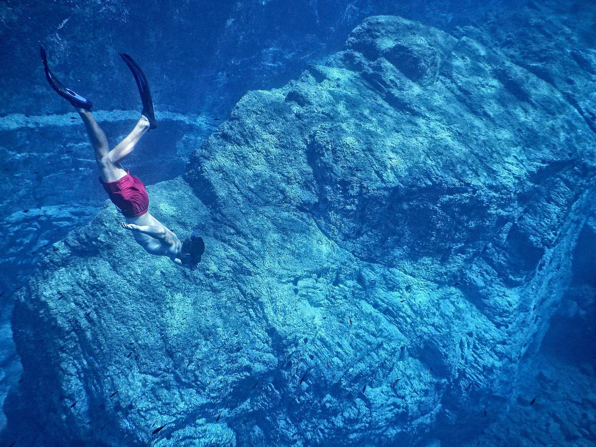 water man in red shorts swimming near huge underwater rock diver