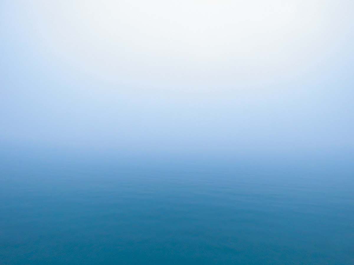 Explore the enchanting beauty of a serene ocean landscape enveloped in fog. This stunning image captures the tranquil blue waters meeting a soft, white sky, creating a dreamlike atmosphere perfect for a variety of projects. Ideal for travel blogs, environmental articles, or as a calming background for wellness content, this scene invites viewers to immerse themselves in the tranquility of nature.