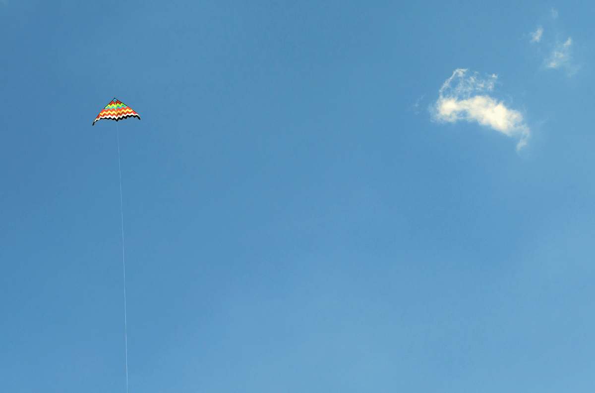 gliding orange and green kite in the sky soaring at daytime leisure activities