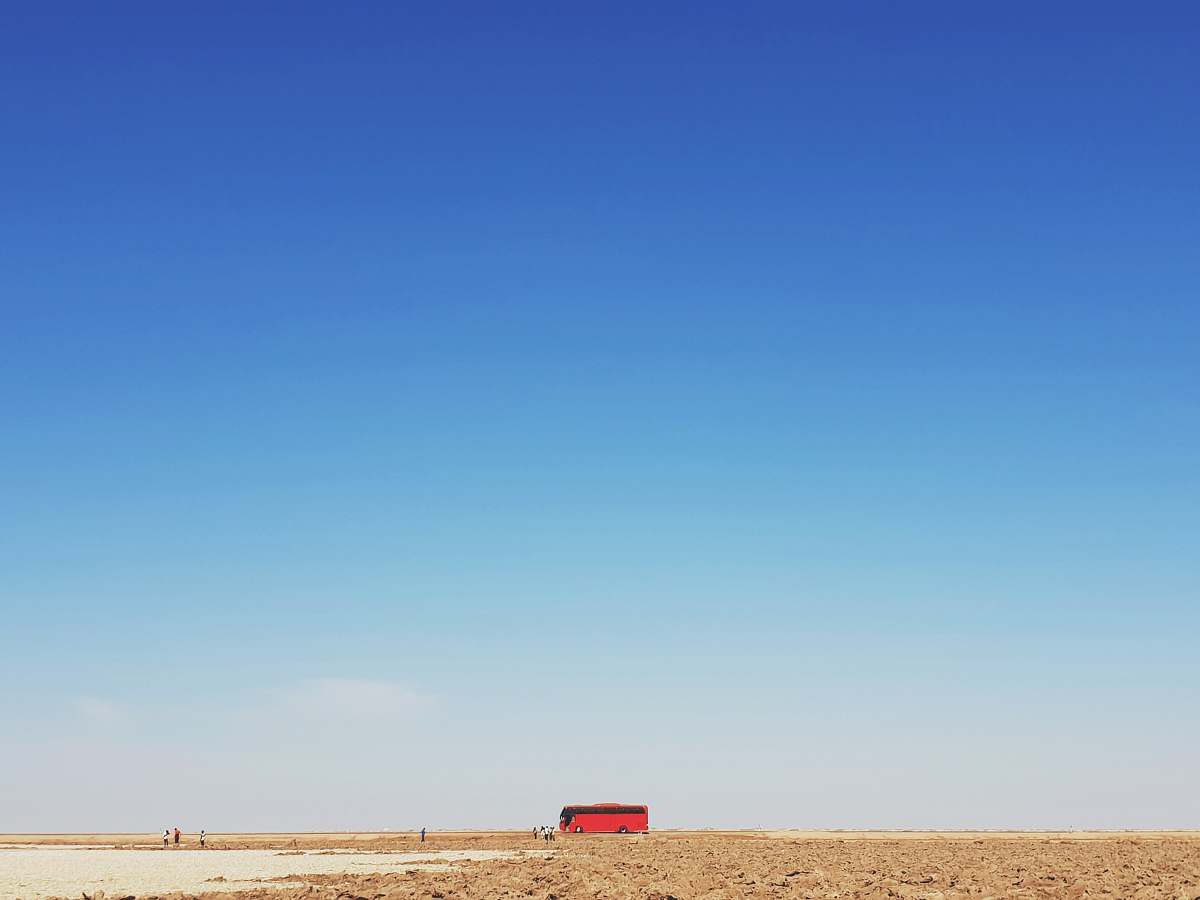 outdoors red bus traveling on brown desert plain nature