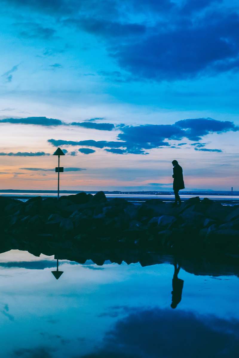 water silhouette of person walking on rocks near body of water reflection