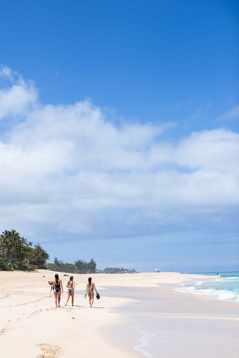 person three women on sea shore under blue and white sky during daytime outdoors