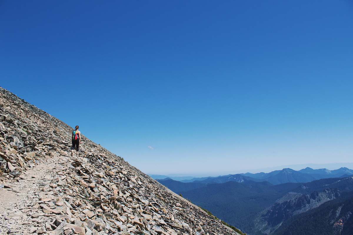 blue landscape photography of man standing on brown mountain mount rainier