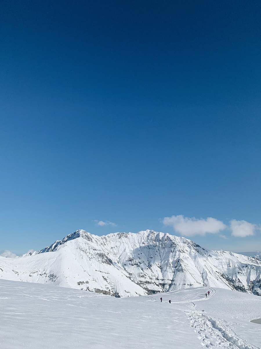 outdoors people standing on snowy field and mountain under blue and white sky during daytime mountain