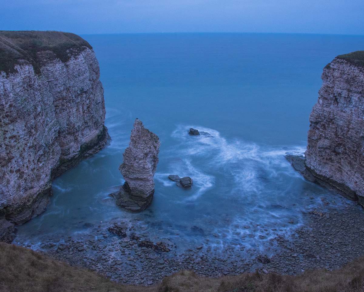 outdoors wavy ocean beside gray rock formation during daytime cliff