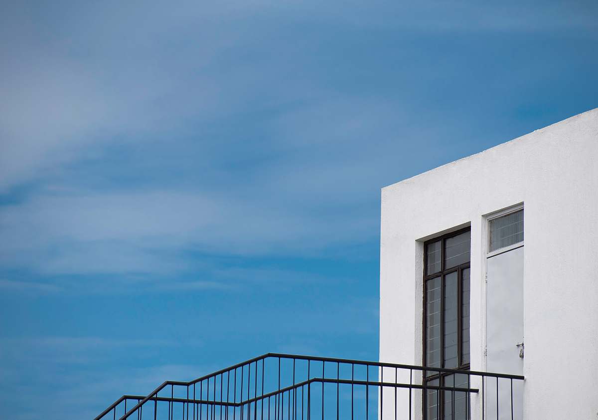banister white building with black staircase under blue sky handrail