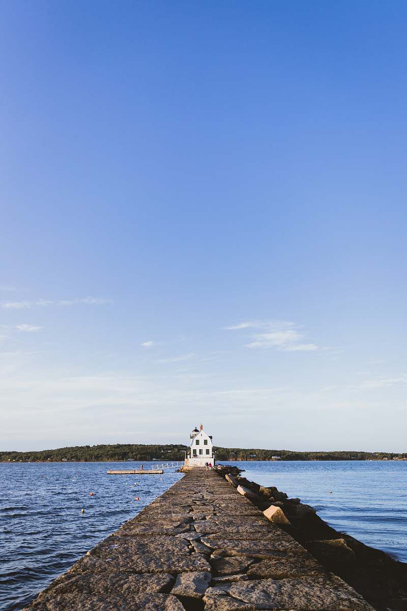ocean landscape photography of grey concrete docking pier with white concrete building at the end of it water