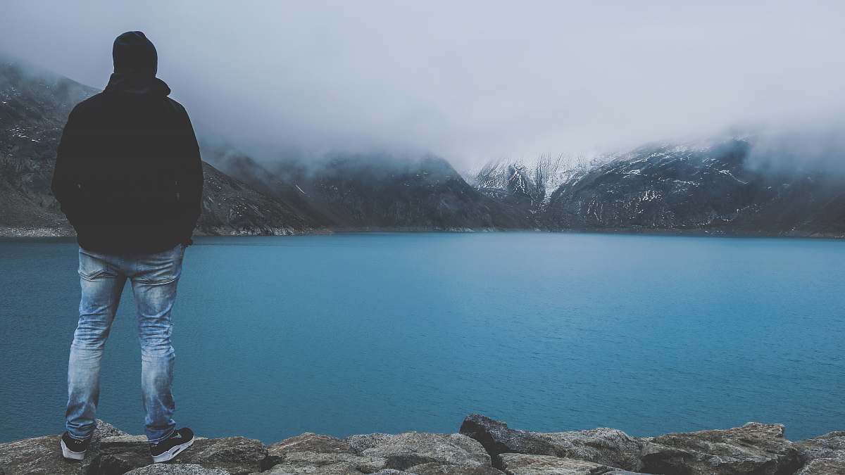 person man standing on cliff facing bod of water lake