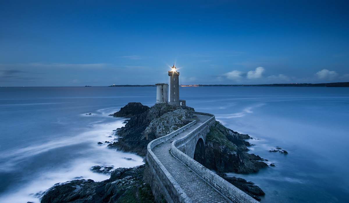 sea gray lighthouse on islet with concrete pathway at daytime coast