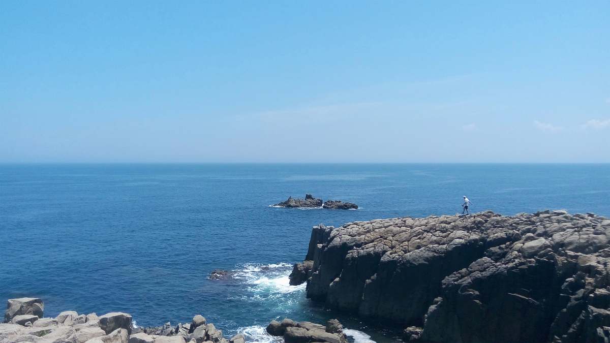 ocean person standing on top of gray stone formation near sea at daytime coast