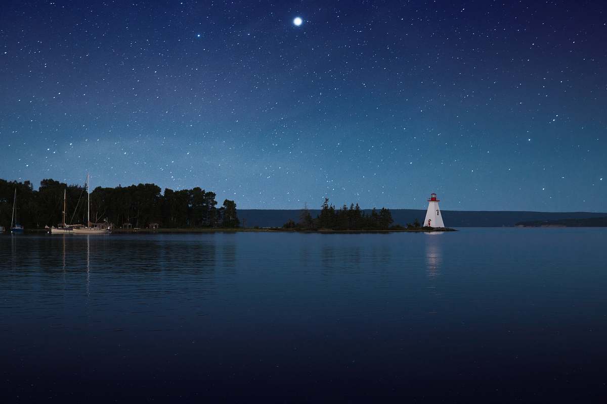 blue photograph of white lighthouse near calm body of water at night canada