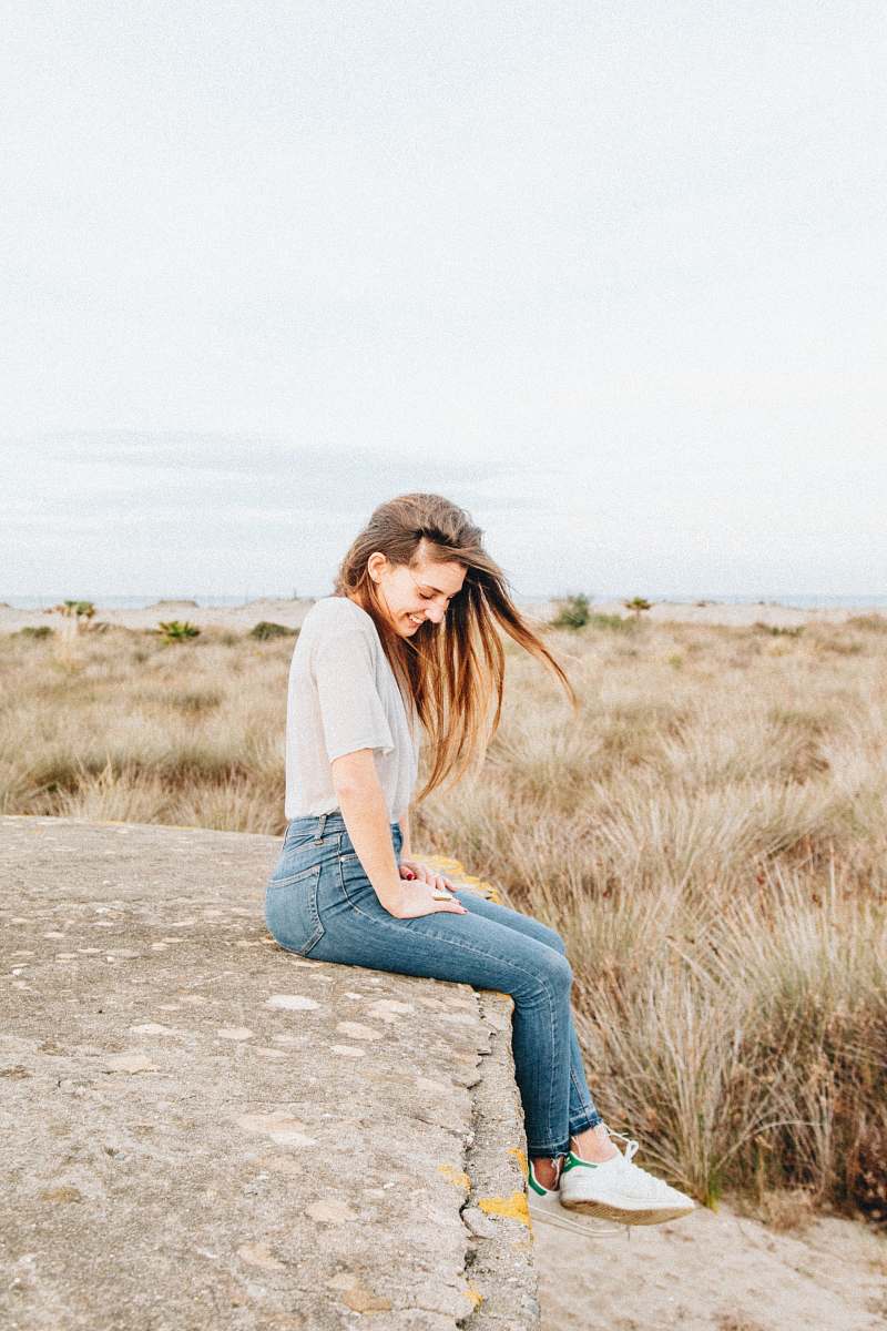 person laughing woman sitting on concrete surrounded by brown grass people