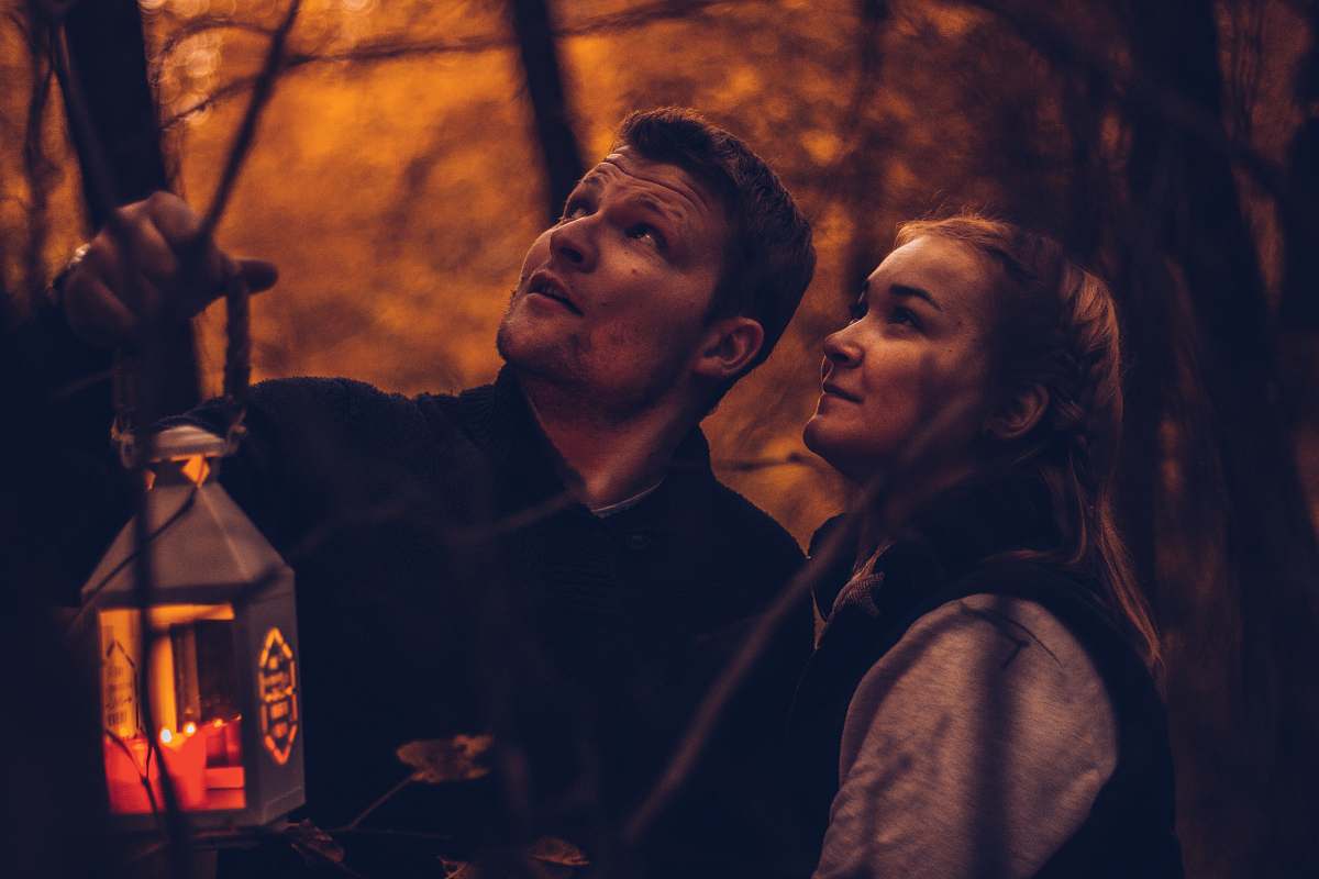 person man carrying candle lantern beside woman both looking at top people