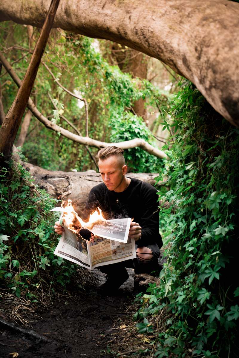 person man in black crew-neck sweater holding burning newspaper outdoors