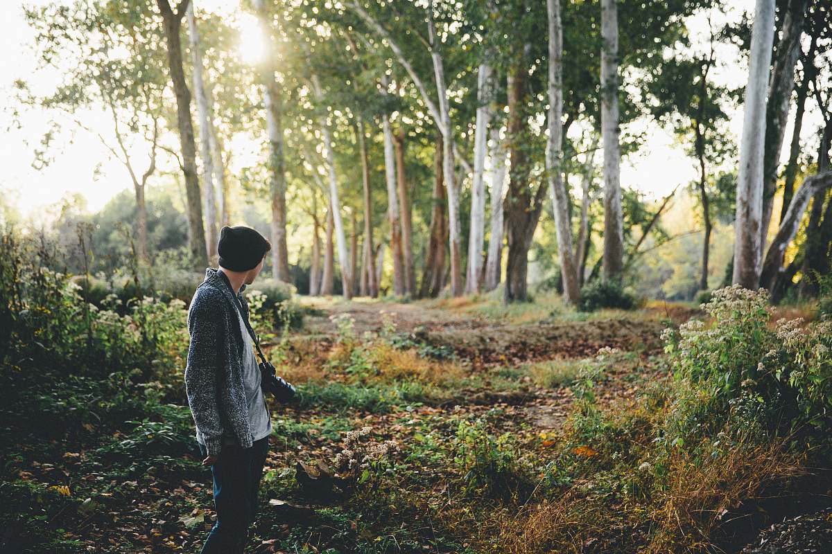 person man with black camera standing near green trees during daytime trees