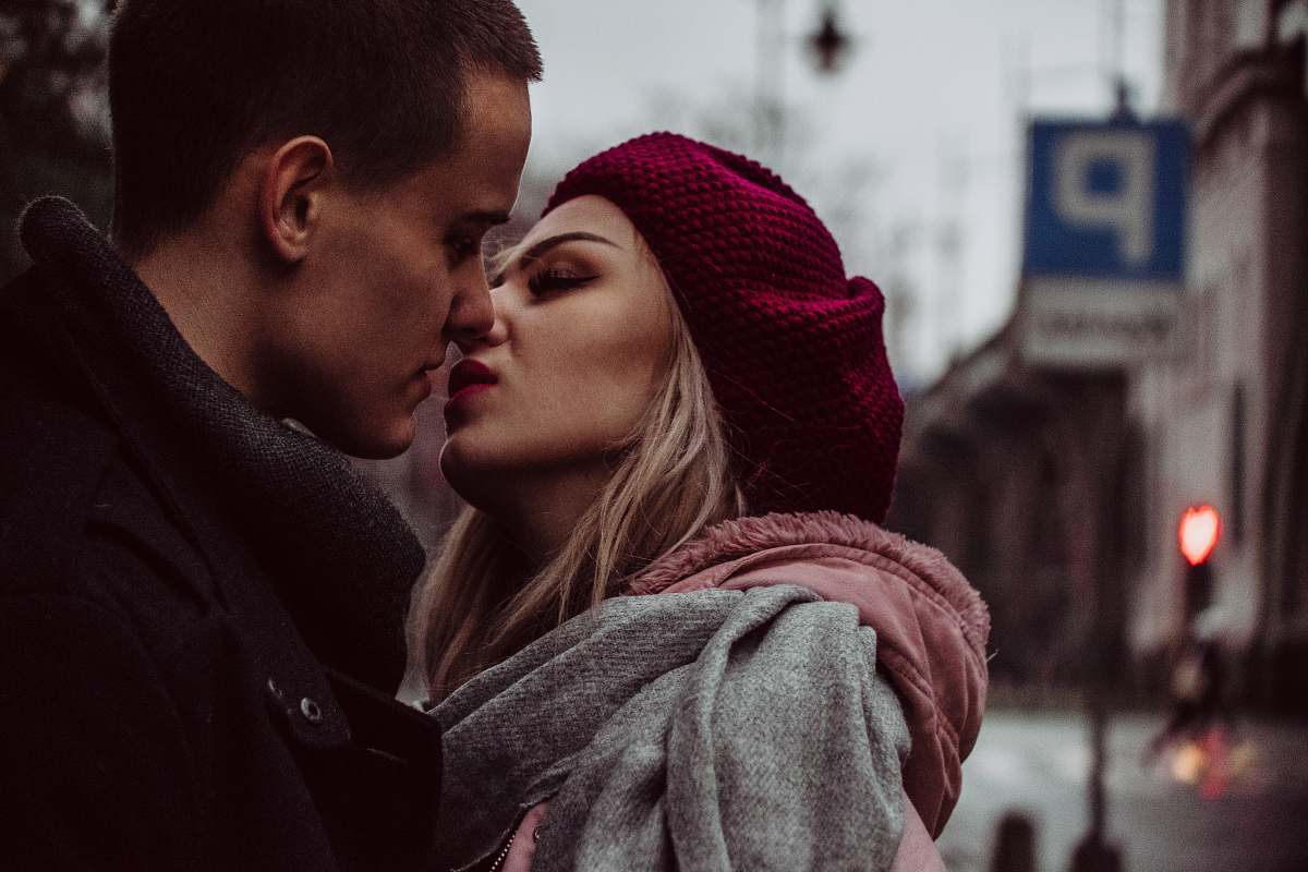 human man and woman standing while kissing beside street signage people