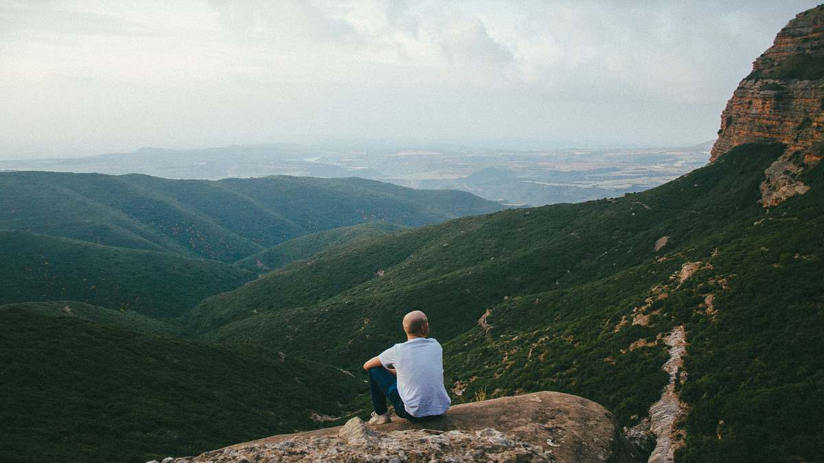 human person sitting on the edge of a cliff over looking mountains during daytime outdoors
