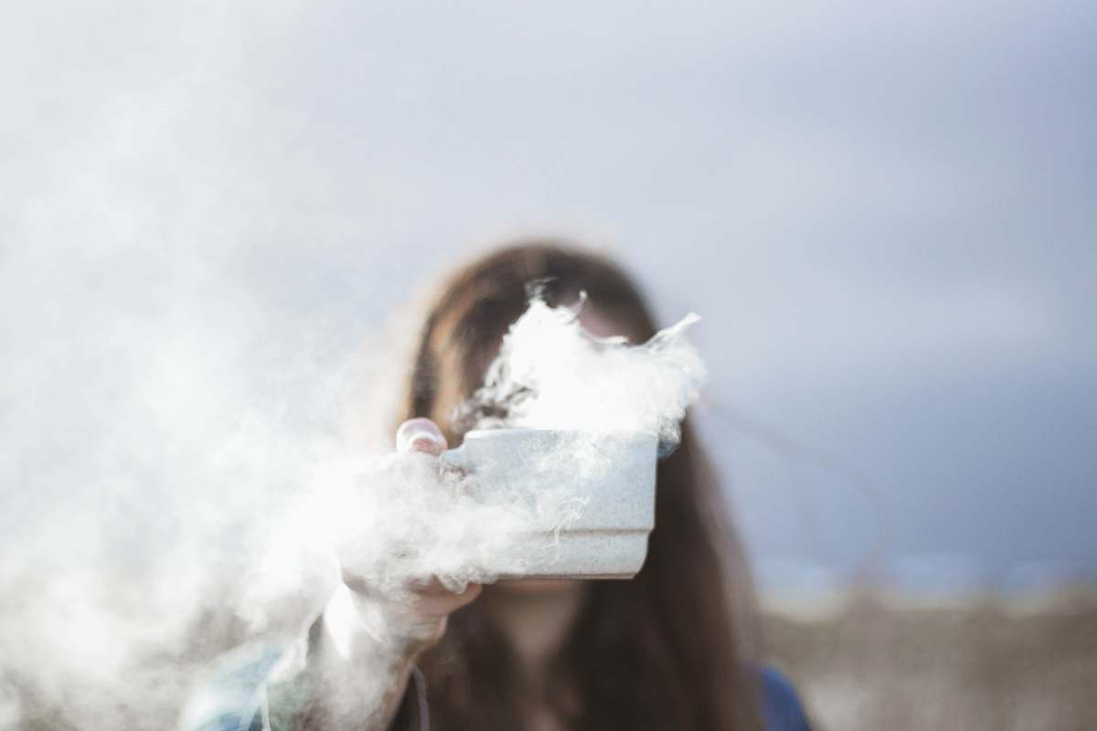 food person holding white ceramic cup with smoke flowing inside teacup