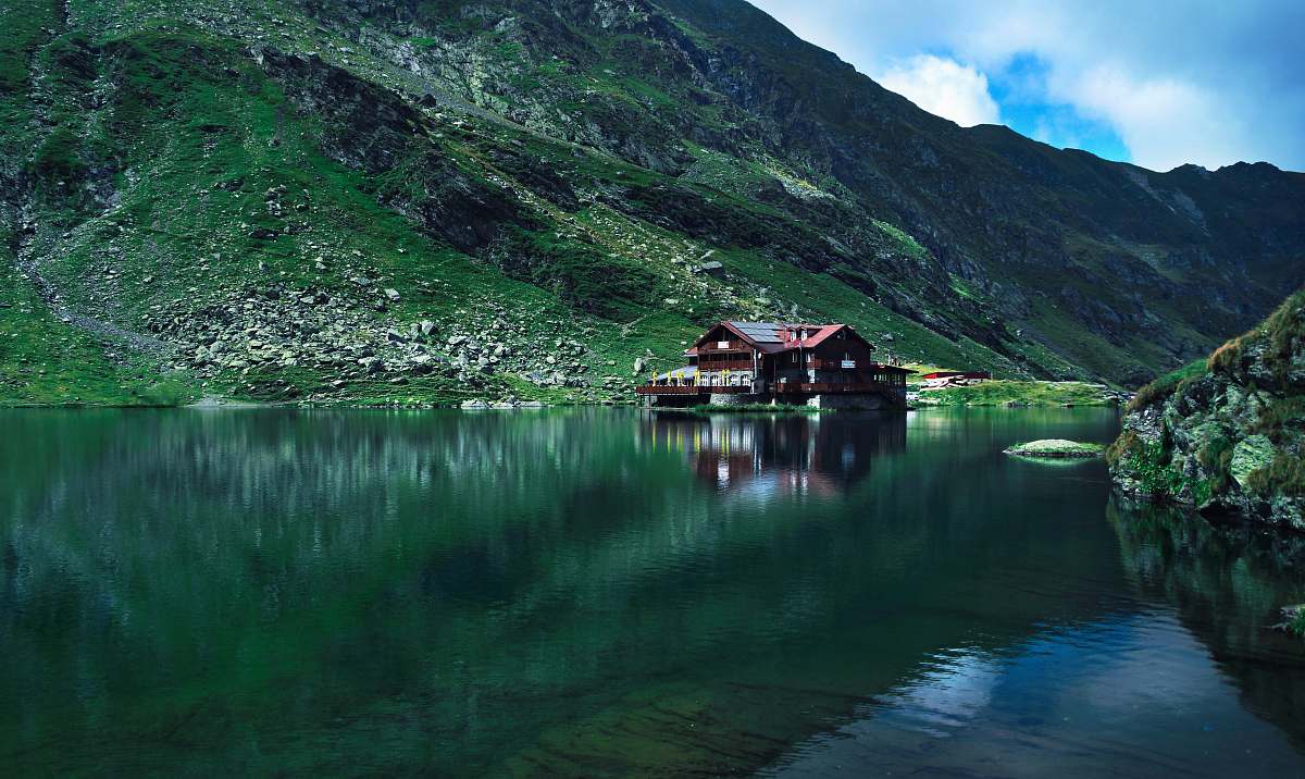 building brown wooden house near mountain surrounded with water at daytime boat