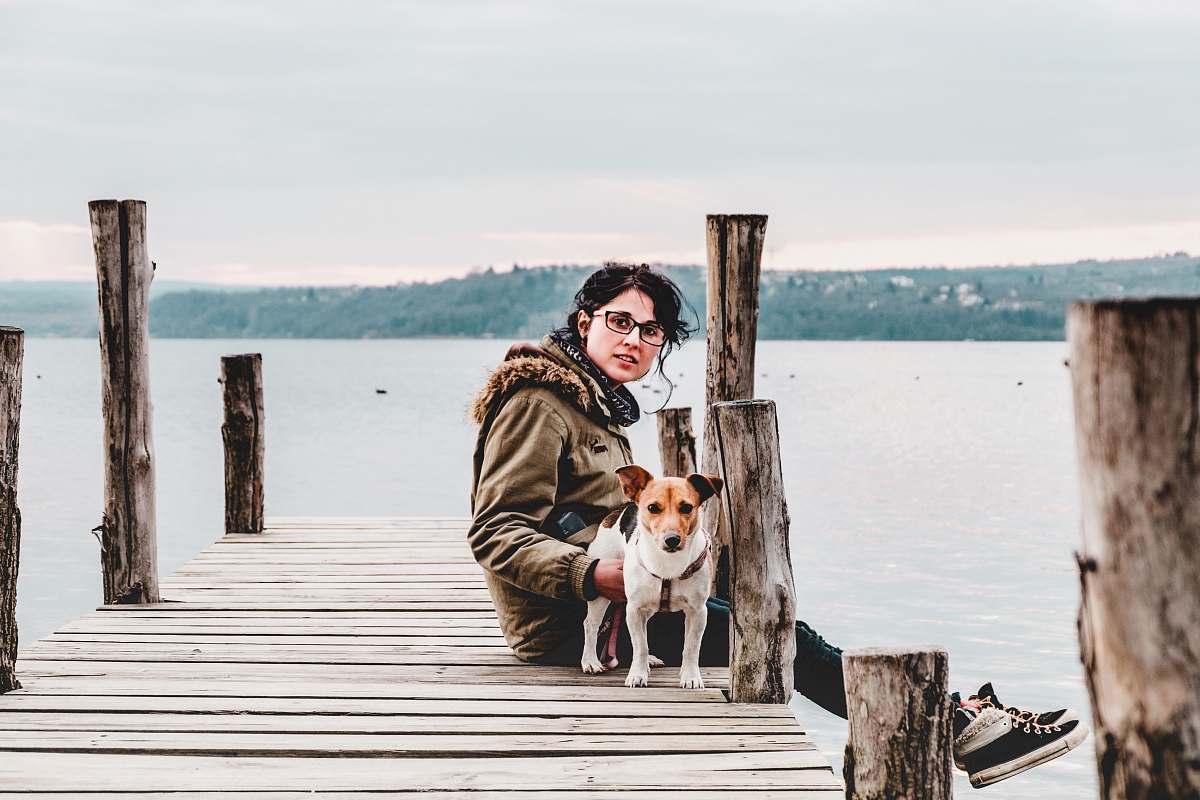 pier woman sitting on brown wooden dock with dog waterfront