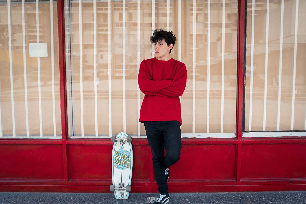 clothing man leaning on glass wall beside leaning skateboard sleeve