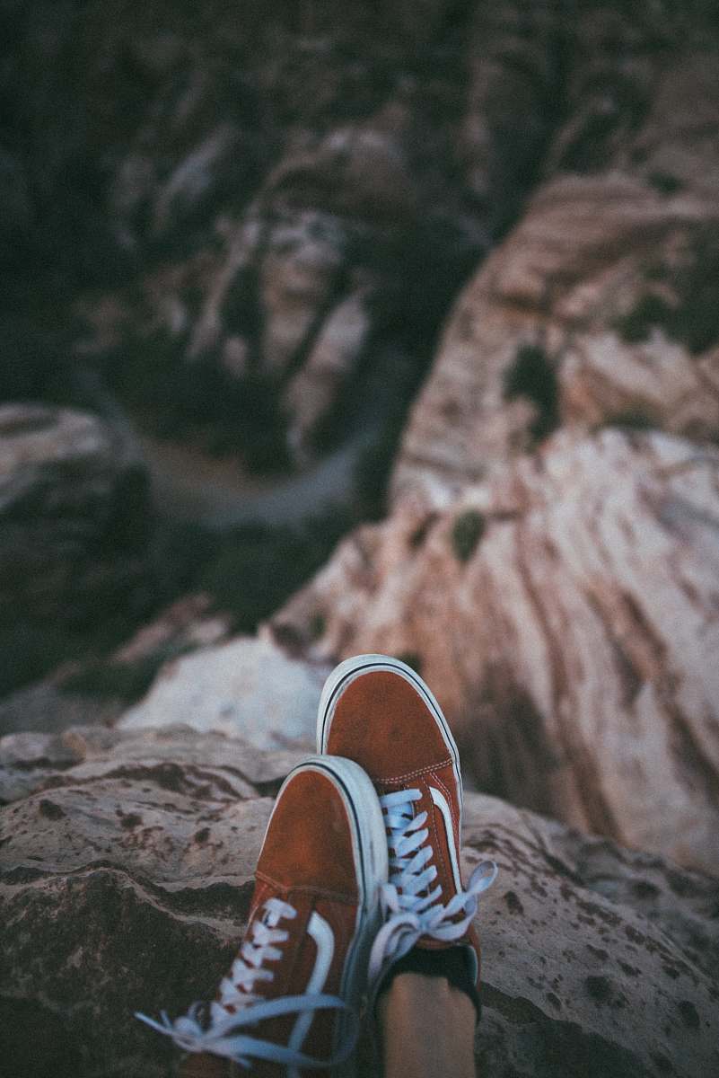 clothing person sitting on cliff wearing brown-and-white Vans low-top sneakers footwear