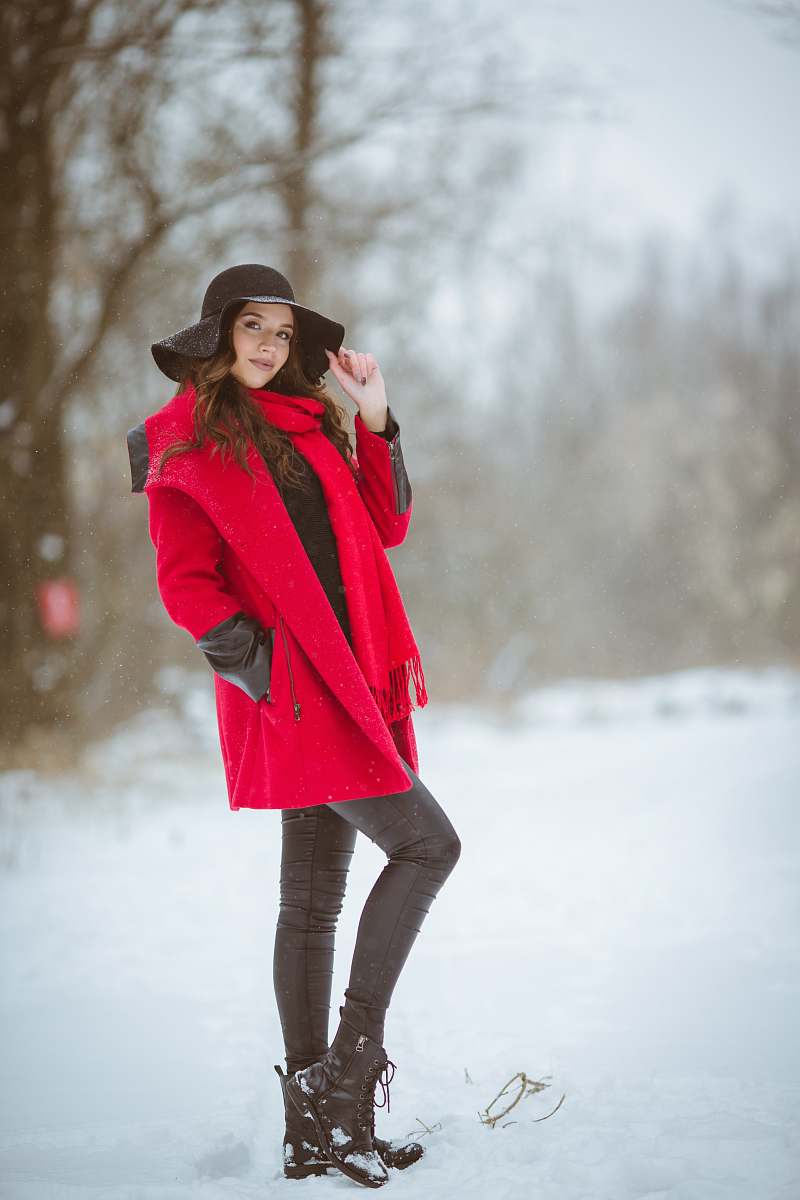 clothing woman in red coat wearing black sunhat smiling while standing on snow-covered ground during daytime coat