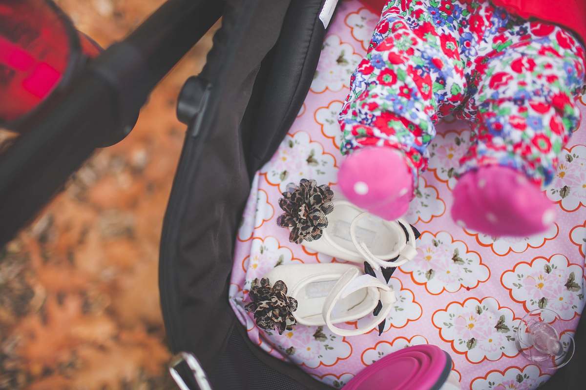 infant pair of white crib shoes on pink and black stroller feet