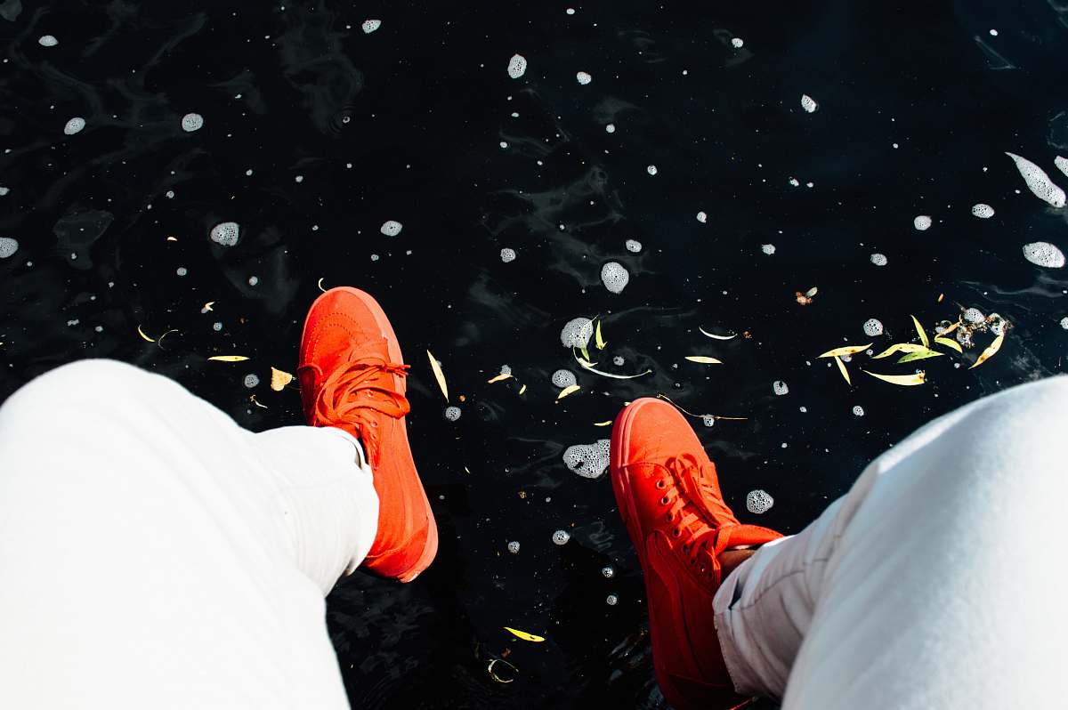 legs person wearing orange sneakers sitting near water shoes