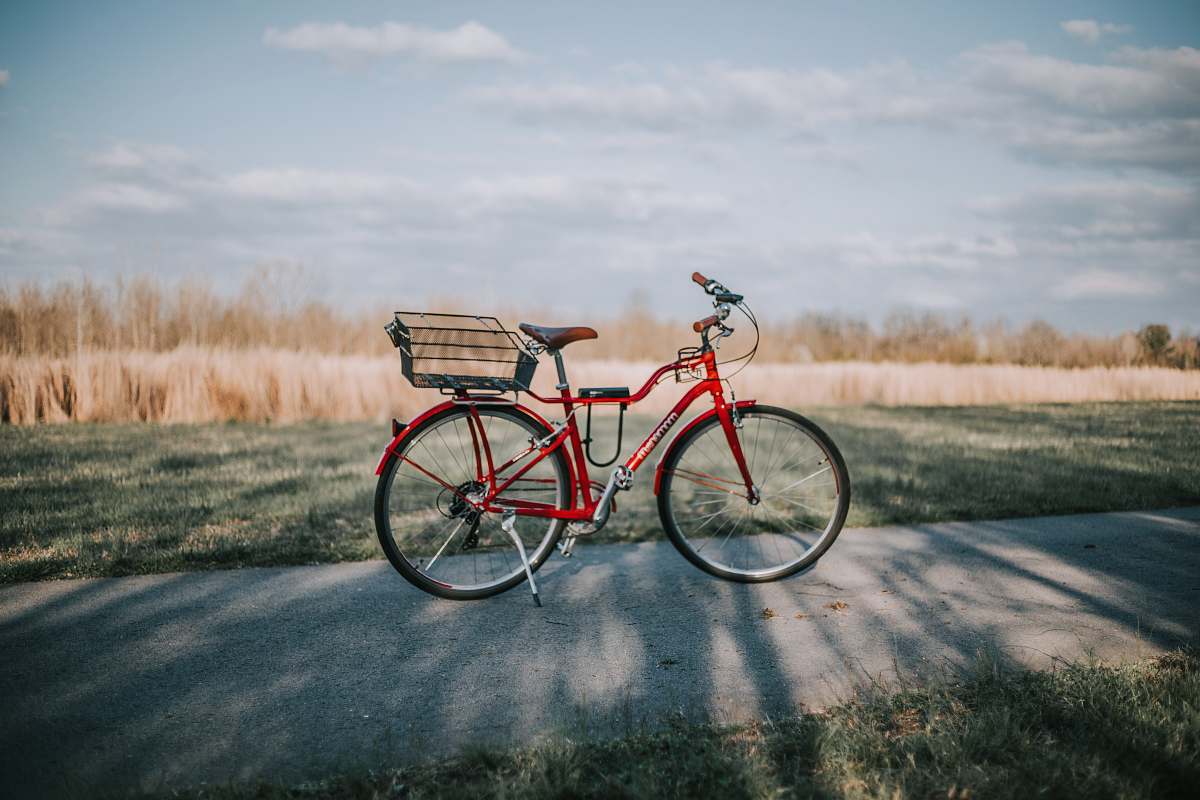 bicycle red commuter bike on road in between grass field during daytime transportation