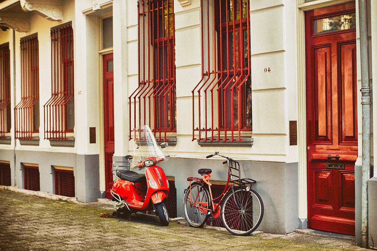 door red motor scooter parked beside house bicycle