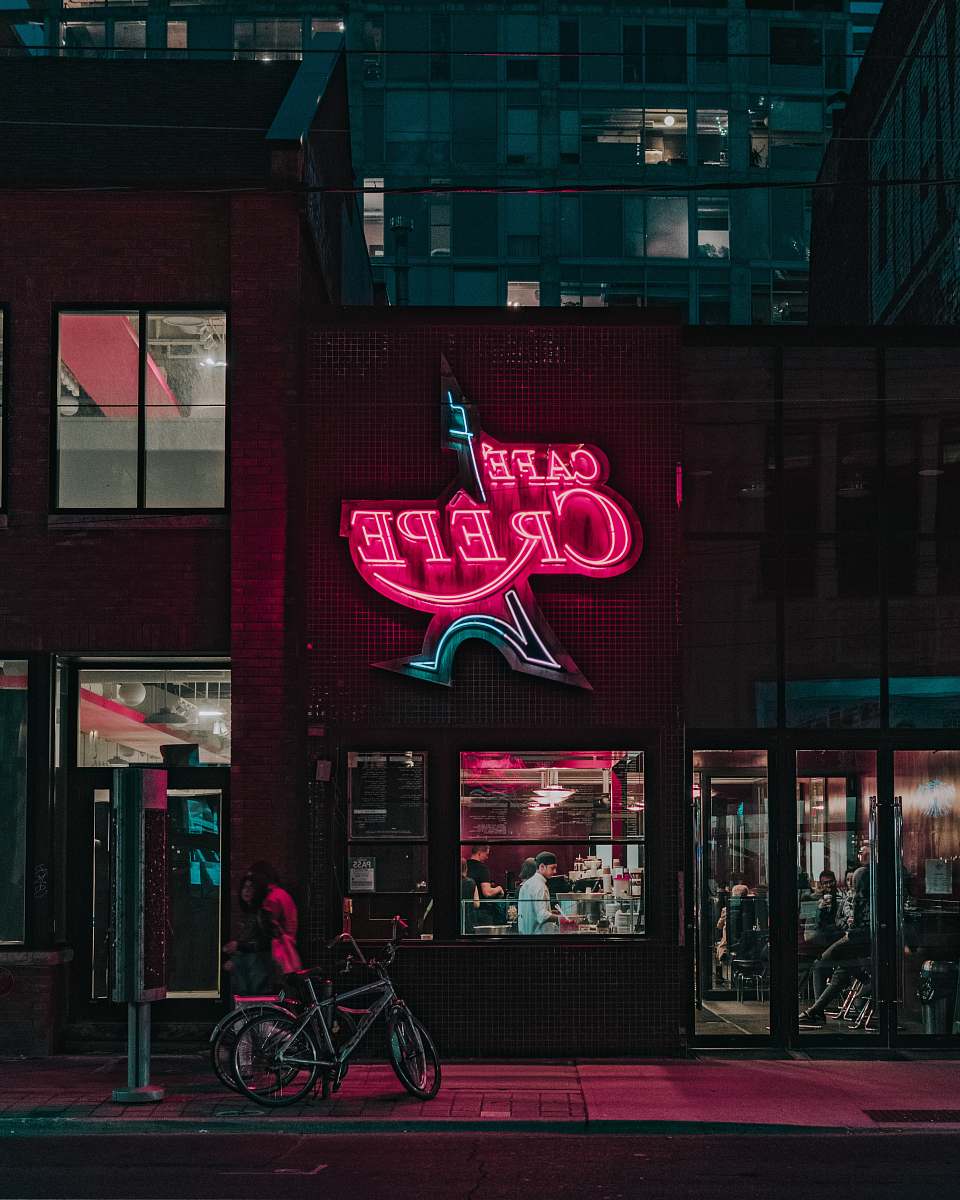 bicycle two people standing in front of Cafe Crepe storefront neon