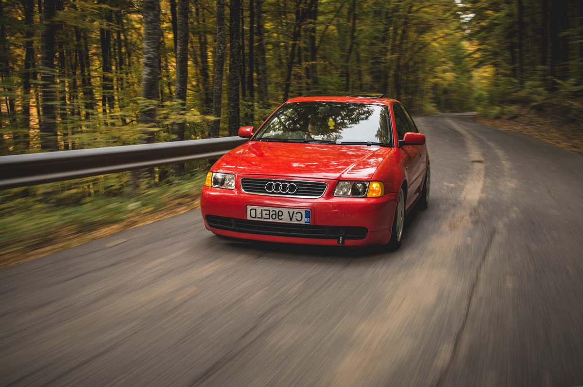 automobile red Audi sedan passing on road between trees during daytime vehicle