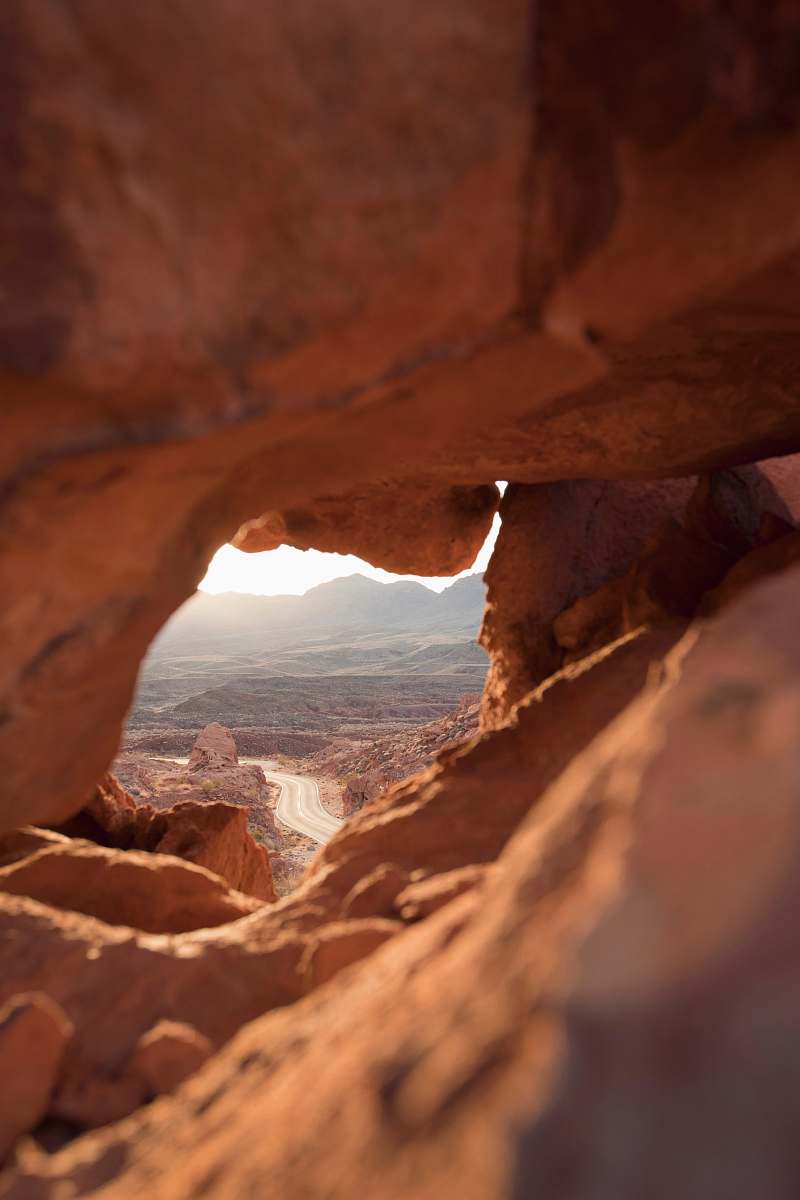nature force perspective photography of brown rock cave overlooking highway at daytime outdoors