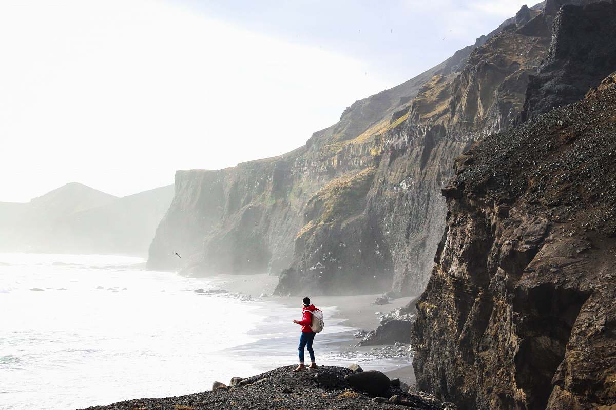 iceland person standing on cliff near body of water during daytime mountain