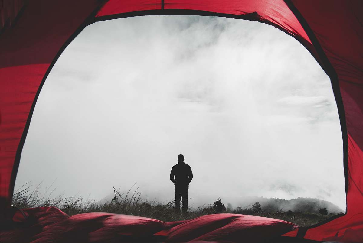 tent man standing on grass field during misty day camping