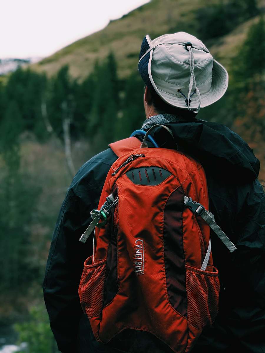 person man in black coat wearing red backpack standing in front of mountain during daytime people