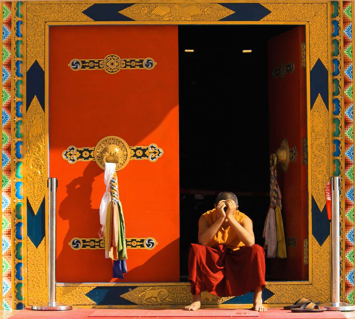 person man in orange top sitting beside door monk