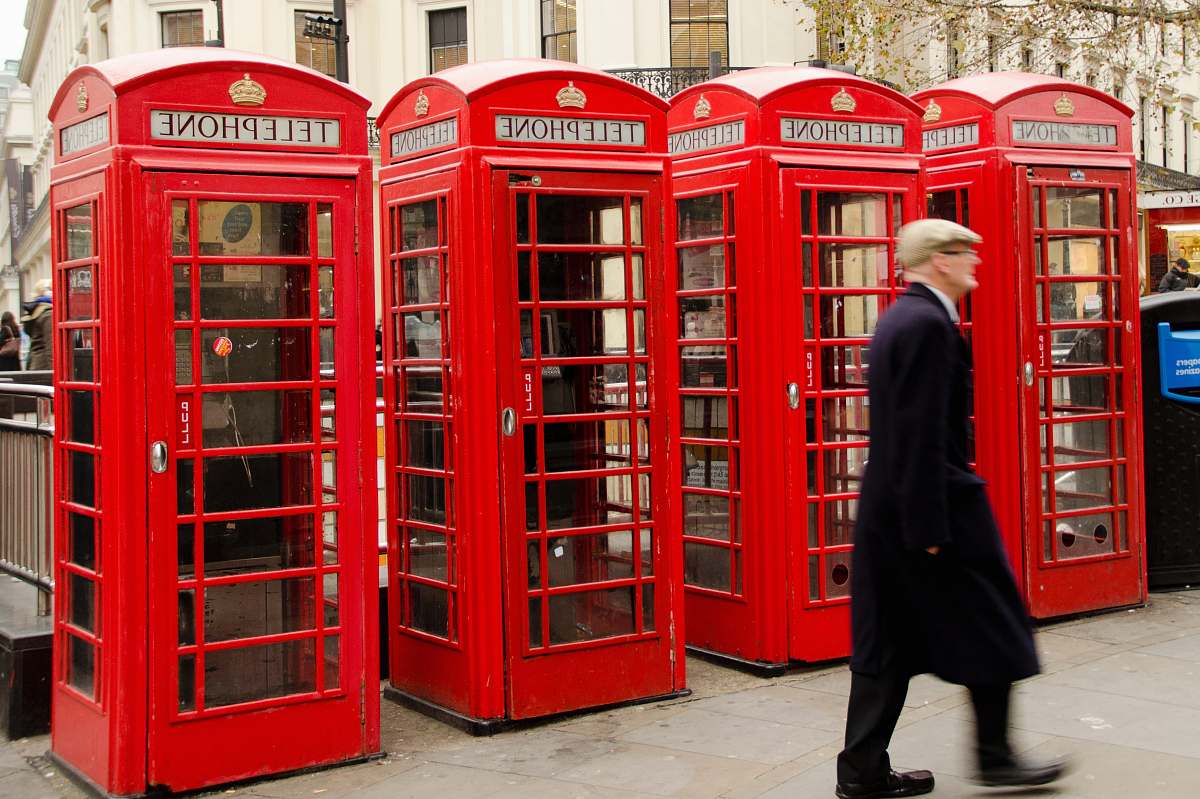 person man walking near red telephone booth during daytime phone booth